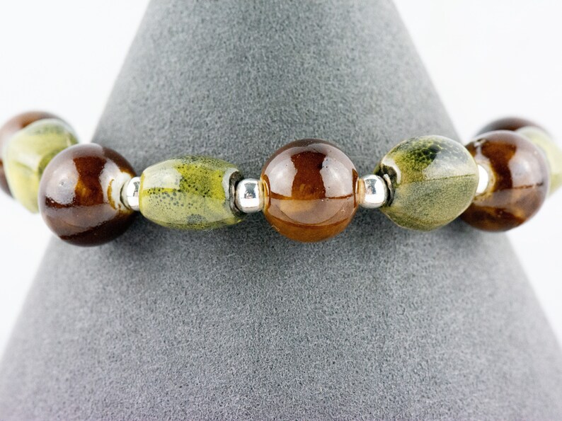 May include: A bracelet made of brown and green ceramic beads with silver spacers.