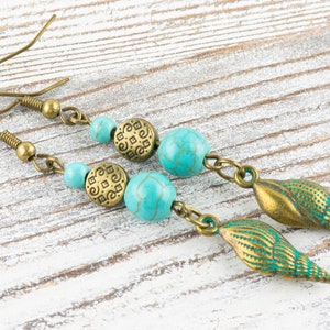 K&ouml;nnte beinhalten: Ein Paar t&uuml;rkisfarbene und bronzene Ohrringe mit einem Muschel-Anh&auml;nger. Die Ohrringe haben t&uuml;rkisfarbene Perlen, bronzene Abstandshalter und einen bronzenen Muschel-Anh&auml;nger.