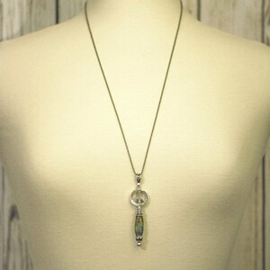 Puede incluir: Un collar con un colgante de plata con el signo de la paz y un abalorio de cuentas verdes y marrones.