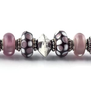 May include: A silver charm bracelet with a variety of beads, including pink, white, and black polka dot beads, and a silver charm in the shape of a diamond.