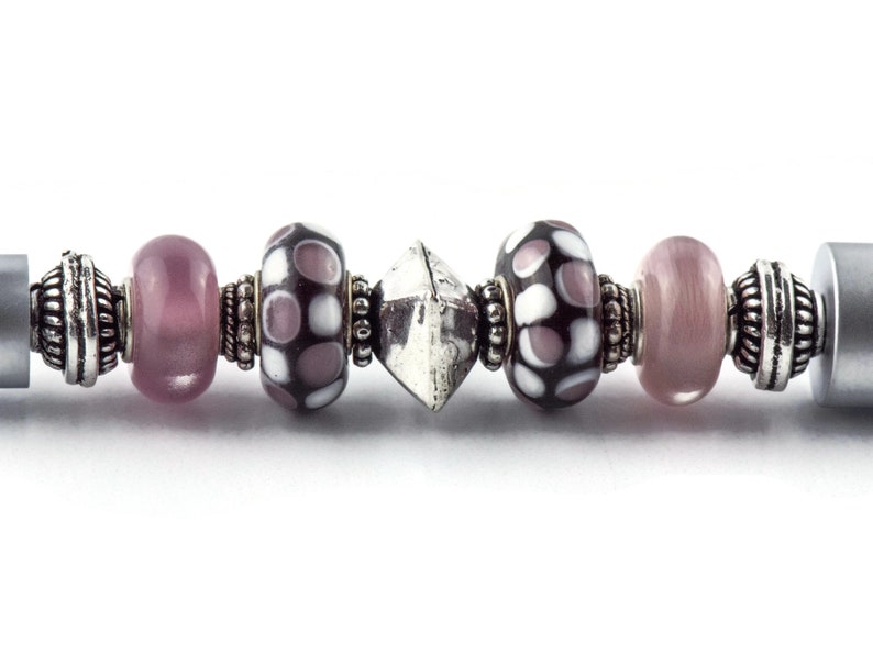 May include: A silver charm bracelet with a variety of beads, including pink, white, and black polka dot beads, and a silver charm in the shape of a diamond.