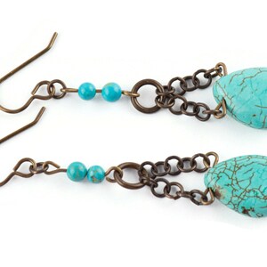 May include: A pair of turquoise dangle earrings with a chain and two small turquoise beads. The earrings have a bronze finish.