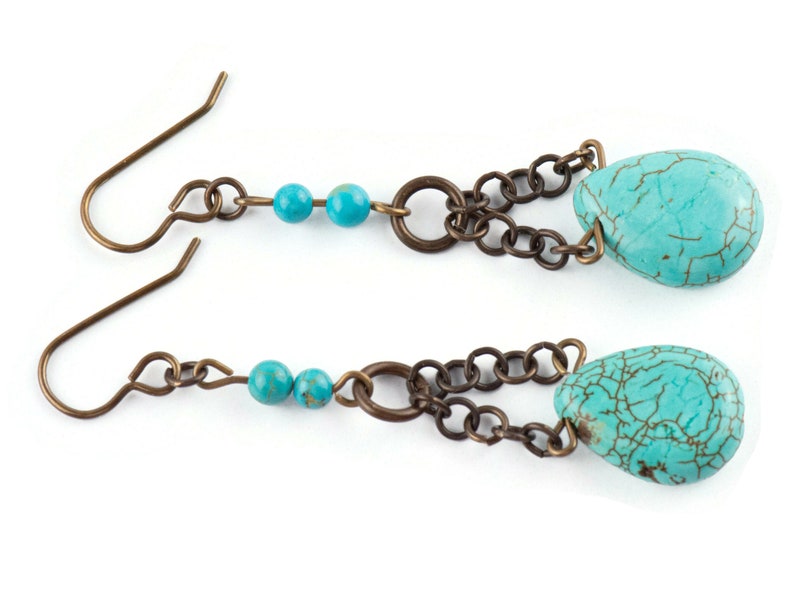 May include: A pair of turquoise dangle earrings with a chain and two small turquoise beads. The earrings have a bronze finish.