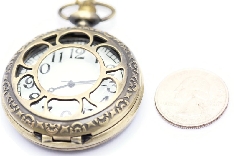 K&ouml;nnte beinhalten: Eine goldfarbene Taschenuhr mit einem verzierten Design und einem wei&szlig;en Zifferblatt. Die Uhr ist etwa so gro&szlig; wie eine deutsche 2-Euro-M&uuml;nze.