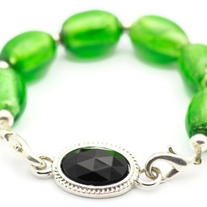 May include: A silver bracelet with a black gemstone and green glass beads.