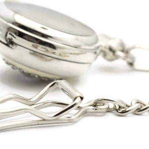 May include: A silver pocket watch with a chain and a clip. The watch has a round face and a silver chain attached to a clip.