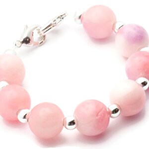 Puede incluir: Una pulsera con cuentas rosas redondas y grandes con espaciadores plateados. Las cuentas var&iacute;an en tonalidad, desde rosa claro hasta rosa intenso, con algunos toques de p&uacute;rpura. La pulsera se asegura con un cierre plateado.