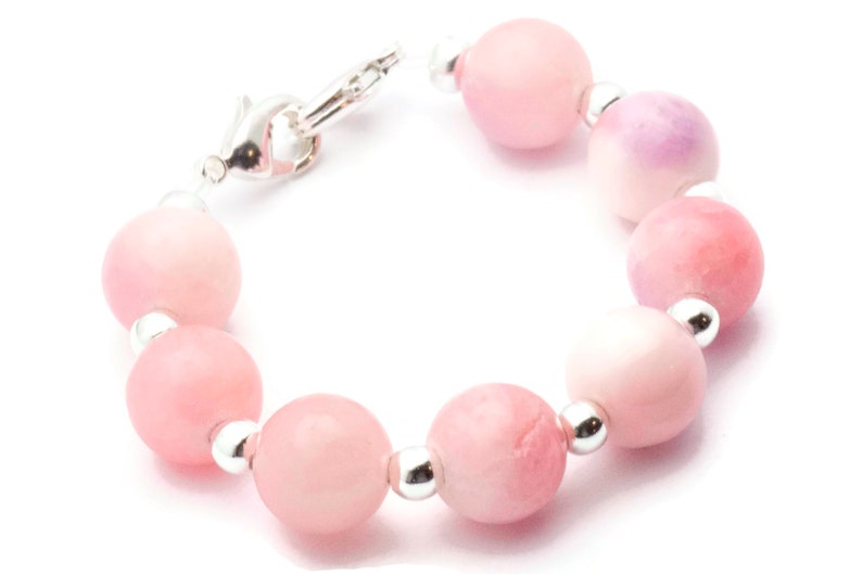 Puede incluir: Una pulsera con cuentas rosas redondas y grandes con espaciadores plateados. Las cuentas var&iacute;an en tonalidad, desde rosa claro hasta rosa intenso, con algunos toques de p&uacute;rpura. La pulsera se asegura con un cierre plateado.