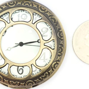 K&ouml;nnte beinhalten: Eine goldfarbene Taschenuhr mit r&ouml;mischen Ziffern auf dem Zifferblatt. Die Uhr hat ein dekoratives, verziertes Design am Rand. Die Uhr ist etwa so gro&szlig; wie eine deutsche 2-Euro-M&uuml;nze.