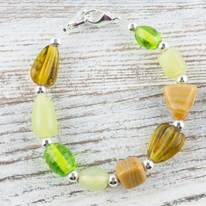 May include: A green, brown and beige beaded bracelet with a silver clasp. The bracelet is made with various shapes and sizes of beads.