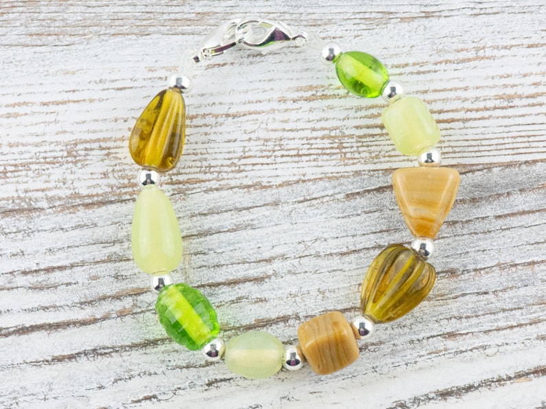May include: A green, brown and beige beaded bracelet with a silver clasp. The bracelet is made with various shapes and sizes of beads.