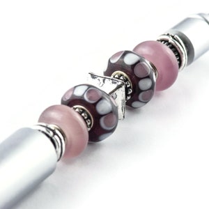 May include: A silver pen with a series of pink and purple glass beads with white polka dots. The beads are separated by silver spacers.