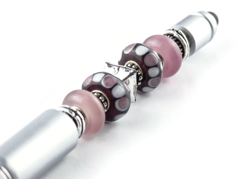 May include: A silver pen with a series of pink and purple glass beads with white polka dots. The beads are separated by silver spacers.
