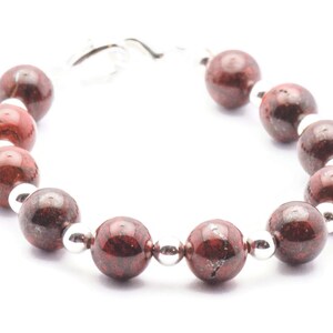 May include: A red and silver beaded bracelet with a silver clasp. The beads are round and have a speckled pattern.