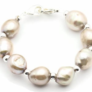 Peut inclure: Un bracelet en argent avec un fermoir et une rang&eacute;e de grosses perles ovales de couleur gris clair.