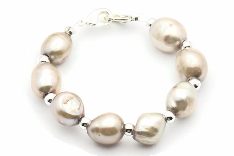 Peut inclure: Un bracelet en argent avec un fermoir et une rang&eacute;e de grosses perles ovales de couleur gris clair.