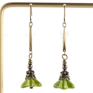 Puede incluir: Un par de pendientes colgantes verdes y dorados con un dije en forma de campana. Los pendientes est&aacute;n hechos de metal y tienen un dise&ntilde;o delicado.