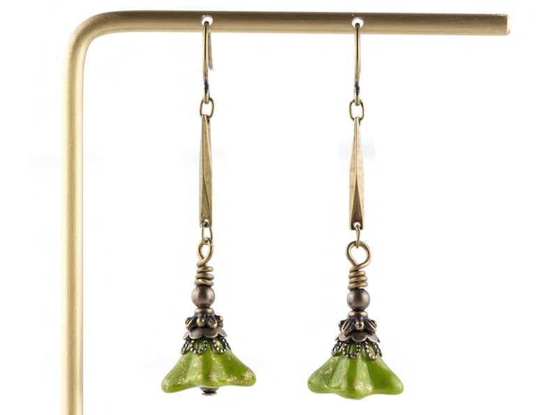 Puede incluir: Un par de pendientes colgantes verdes y dorados con un dije en forma de campana. Los pendientes est&aacute;n hechos de metal y tienen un dise&ntilde;o delicado.