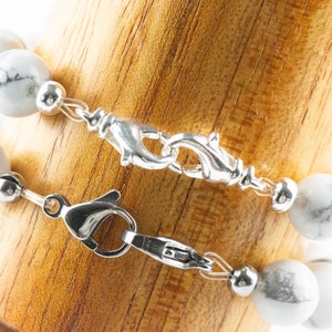 Peut inclure: Deux bracelets en perles d'howlite blanche avec des fermoirs &agrave; ressort en argent. Les bracelets sont superpos&eacute;s sur une surface en bois.