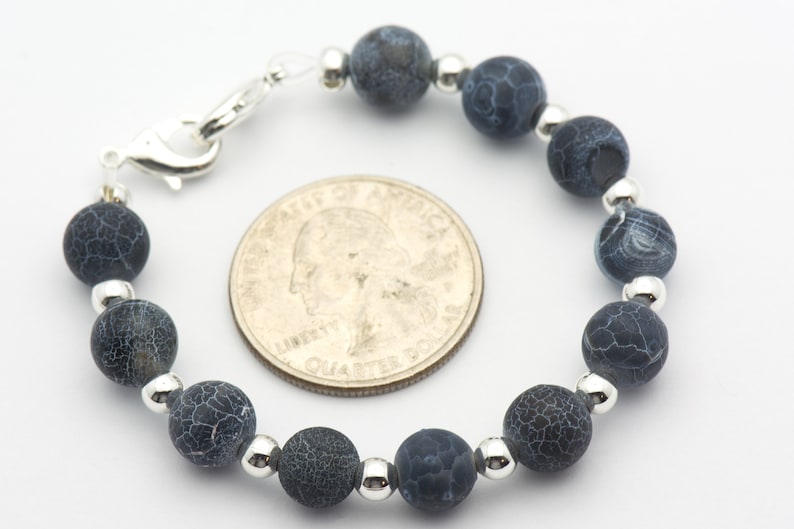 May include: A blue agate bead bracelet with silver spacers and a silver clasp. The bracelet is about the size of a quarter.