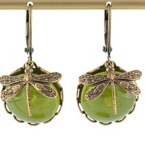 May include: A pair of green glass dangle earrings with a dragonfly charm. The earrings have a brass finish and a delicate design.