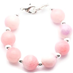 Puede incluir: Pulsera de cuentas con cuentas redondas de color rosa claro y blanco. Las cuentas est&aacute;n ensartadas con peque&ntilde;as cuentas de metal plateado. La pulsera tiene un cierre plateado.