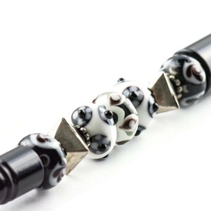 May include: A black pen with a silver and black patterned cap and a series of white and black glass beads with silver accents.