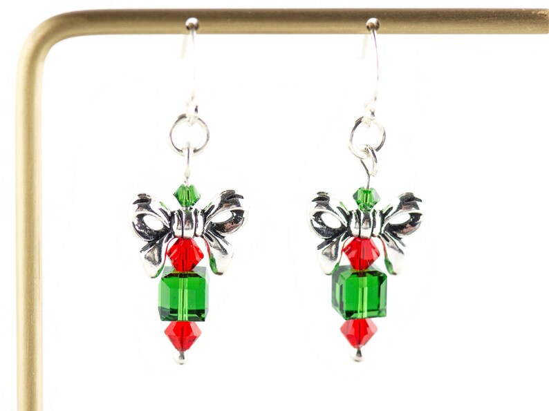 Pode incluir: Brincos de prata com um design de la&ccedil;o e cubo de cristal verde e vermelho. Os brincos est&atilde;o em um expositor.