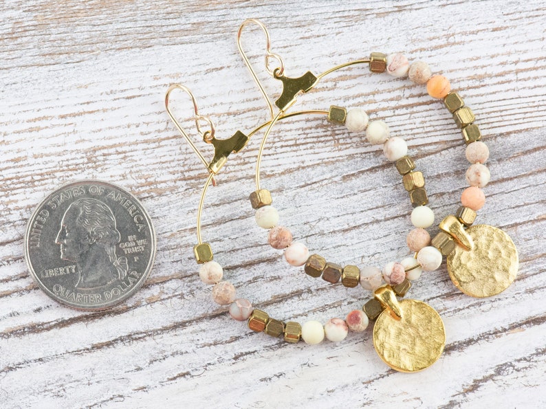May include: Gold hoop earrings with a hammered gold disc charm and a mix of beige, white, and peach colored beads.