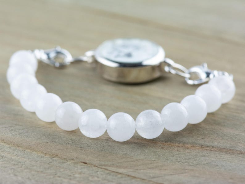 May include: A white beaded bracelet with a silver watch attached. The bracelet is made of round, white beads and the watch has a silver face and hands.