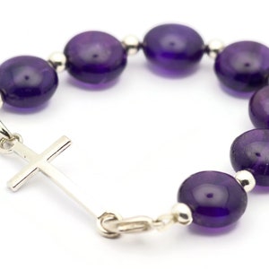 May include: A purple amethyst beaded bracelet with a silver cross charm.