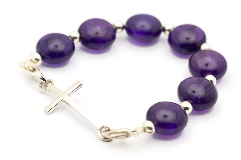 May include: A purple amethyst beaded bracelet with a silver cross charm.