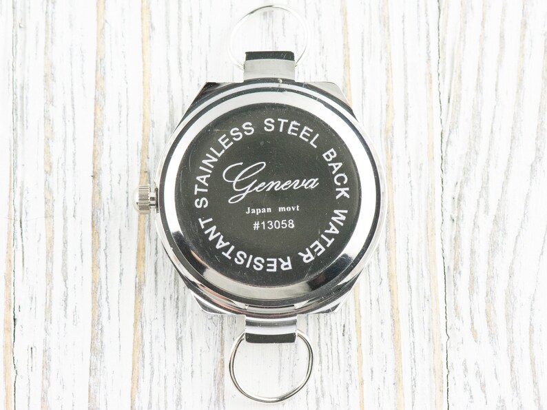 May include: The back of a silver watch with a black face. The watch has the words "Stainless Steel Back Water Resistant" and "Geneva Japan movt #13058" printed on the back.