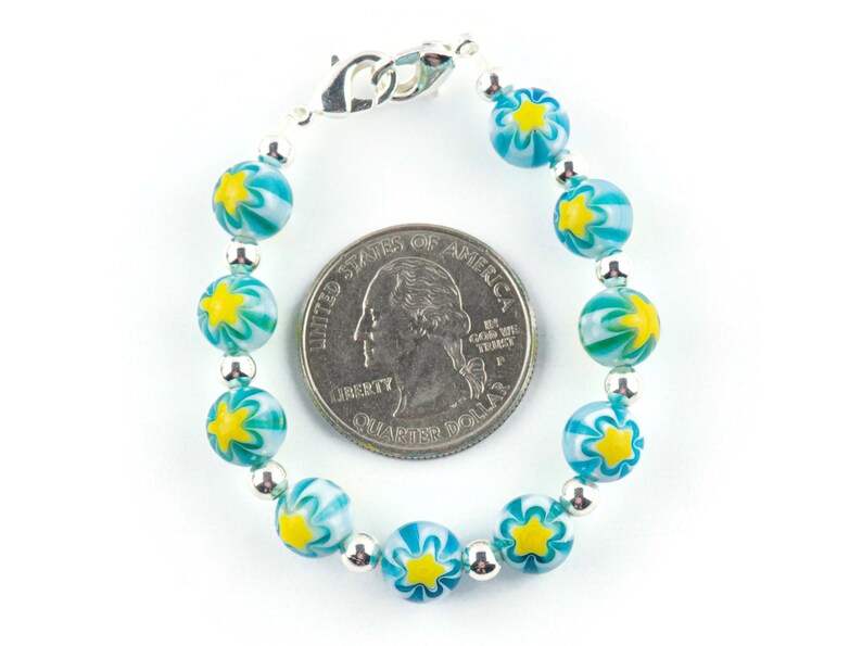 Peut inclure: Un bracelet en argent avec des perles en forme d'&eacute;toile bleues et jaunes. Le bracelet est &agrave; peu pr&egrave;s de la taille d'une pi&egrave;ce de 25 cents am&eacute;ricaine.