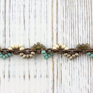 May include: A beaded chain bracelet with brown metal links and alternating clusters of white, beige, and light blue beads.