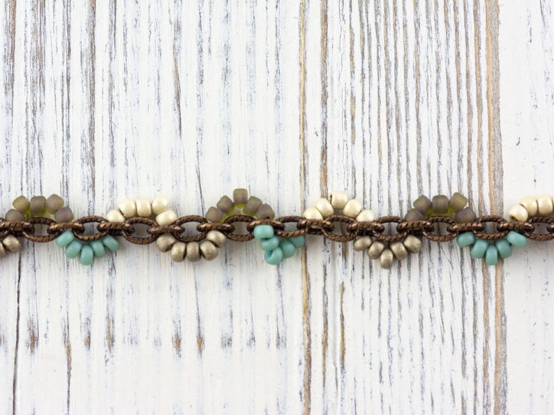 May include: A beaded chain bracelet with brown metal links and alternating clusters of white, beige, and light blue beads.