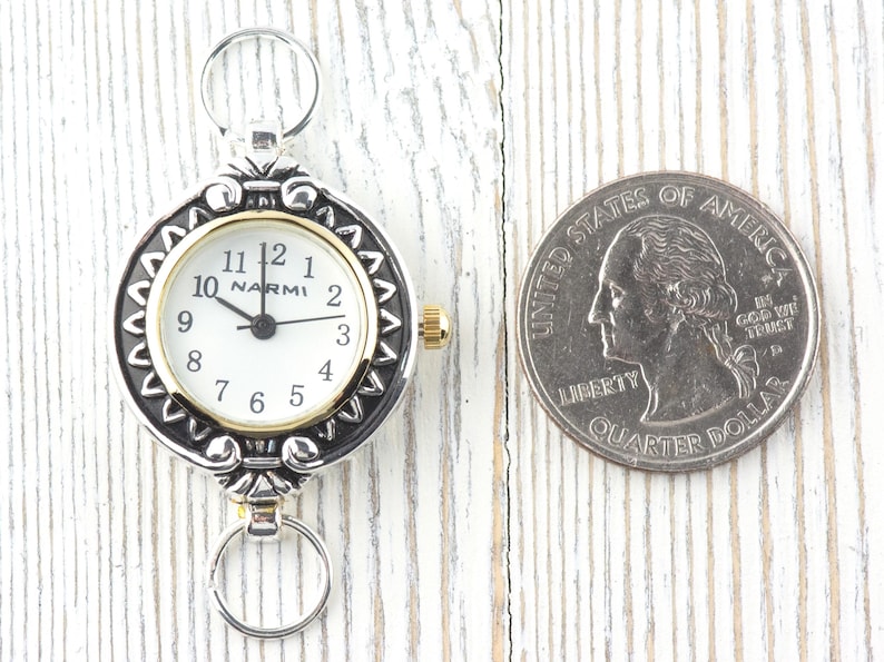 Pu&ograve; includere: Un orologio da tasca argentato e dorato con quadrante bianco e numeri neri. L'orologio ha un anello in alto e in basso per l'attacco. Una moneta da un quarto di dollaro &egrave; accanto all'orologio per il confronto delle dimensioni.
