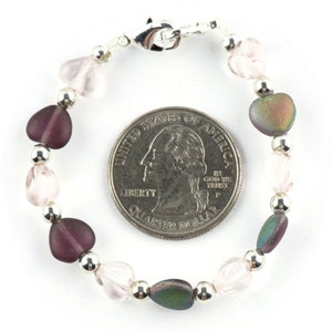 May include: A silver heart charm bracelet with pink, purple, and iridescent heart beads. The bracelet is about the size of a quarter.