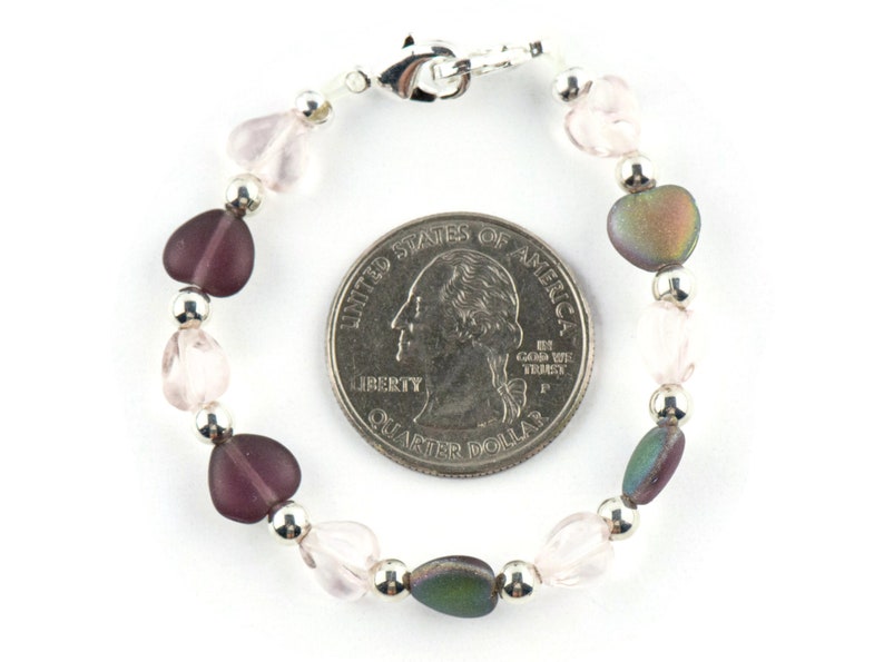 May include: A silver heart charm bracelet with pink, purple, and iridescent heart beads. The bracelet is about the size of a quarter.