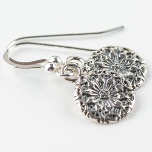 May include: Silver dangle earrings with a floral design. The earrings are made of sterling silver and have a delicate, feminine look.