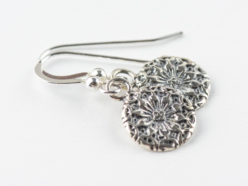 May include: Silver dangle earrings with a floral design. The earrings are made of sterling silver and have a delicate, feminine look.
