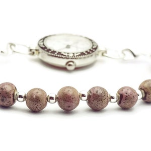 May include: A silver watch with a white face and black markings is attached to a bracelet made of brown beads.