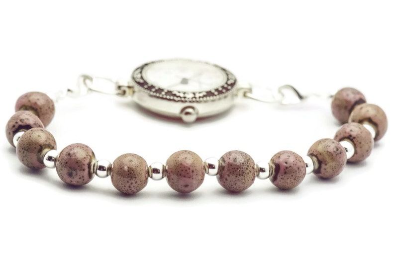 May include: A silver watch with a white face and black markings is attached to a bracelet made of brown beads.