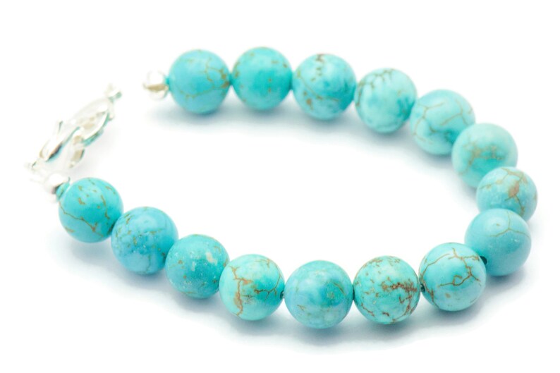 May include: A turquoise beaded bracelet with a silver clasp. The beads are round and have a marbled pattern.