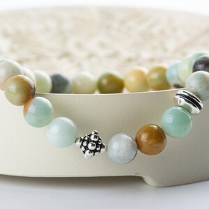 Black Gold Amazonite Genuine Gemstone Stretch Bracelet displayed on a decorative bowl. Amazonite beads are multicolor earth-tones. Center bead is a silver Bali style bead. Bracelet hangs slightly over side edge of decorative bowl.