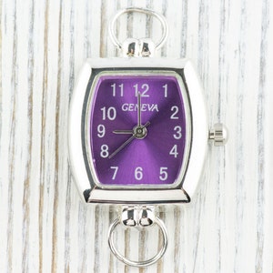 May include: A silver watch with a purple face and white numbers. The watch has a square shape with rounded corners and a loop on the top.