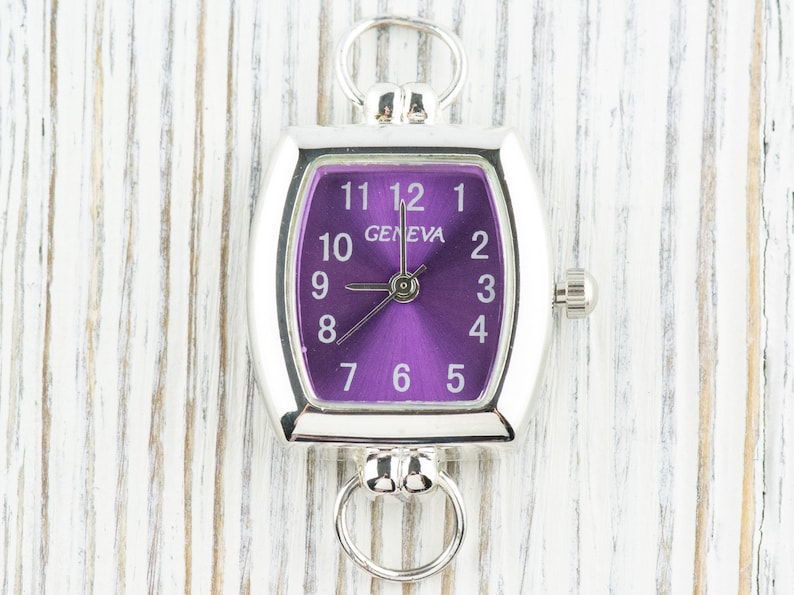 May include: A silver watch with a purple face and white numbers. The watch has a square shape with rounded corners and a loop on the top.