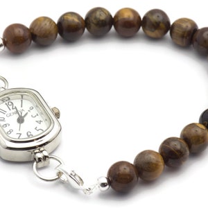 Op de afbeelding: Een zilveren horloge met een vierkante wijzerplaat en bruine tijgeroog kralen bevestigd aan een zilveren ketting.