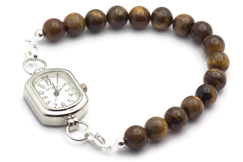 Op de afbeelding: Een zilveren horloge met een vierkante wijzerplaat en bruine tijgeroog kralen bevestigd aan een zilveren ketting.