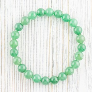 May include: A green gemstone bracelet made of round beads. The bracelet is laid out on a white wooden surface.